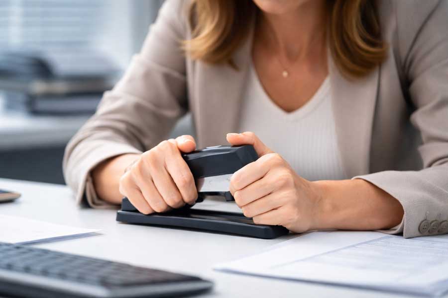 Une femme stressée au bureau tient une agrafeuse entre ses mains.